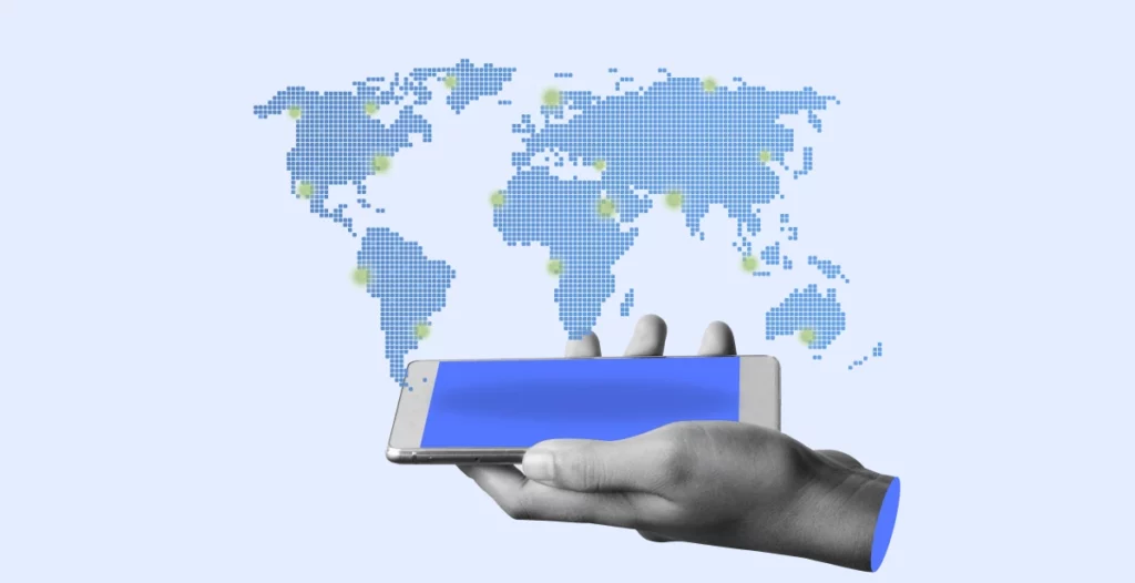 Mapa de mundo en color azul y países marcados en verde, mientras una mano está sosteniendo un celular con la pantalla en azúl.  