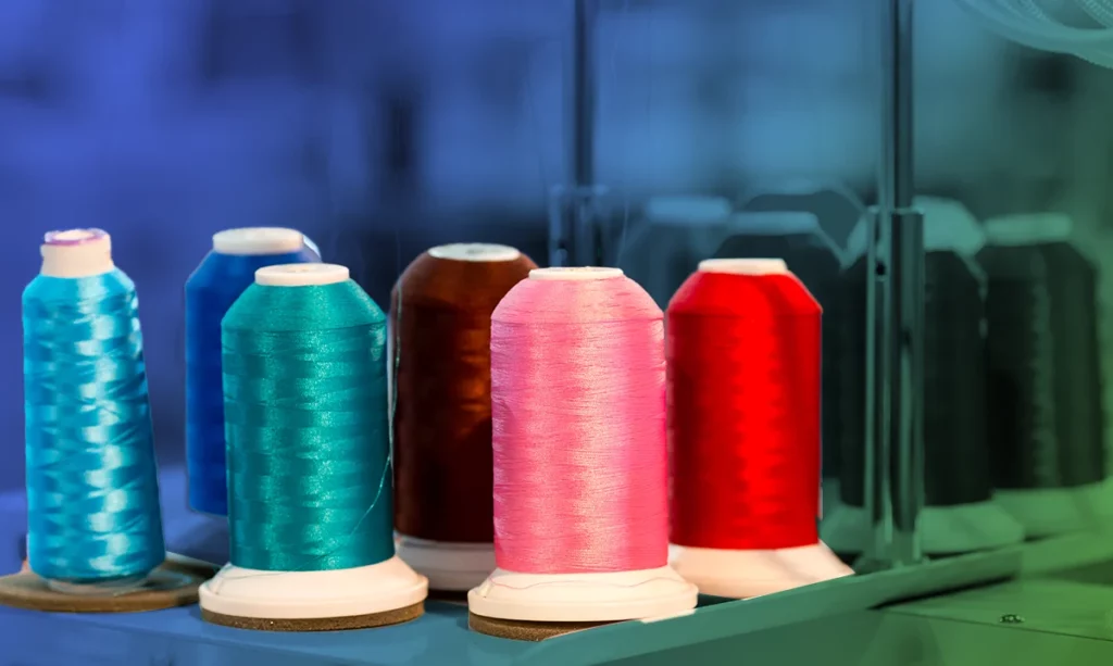 A vibrant array of thread spools in teal, blue, brown, pink, and red on a manufacturing line, symbolizing the fashion industry's diverse and dynamic production processes.