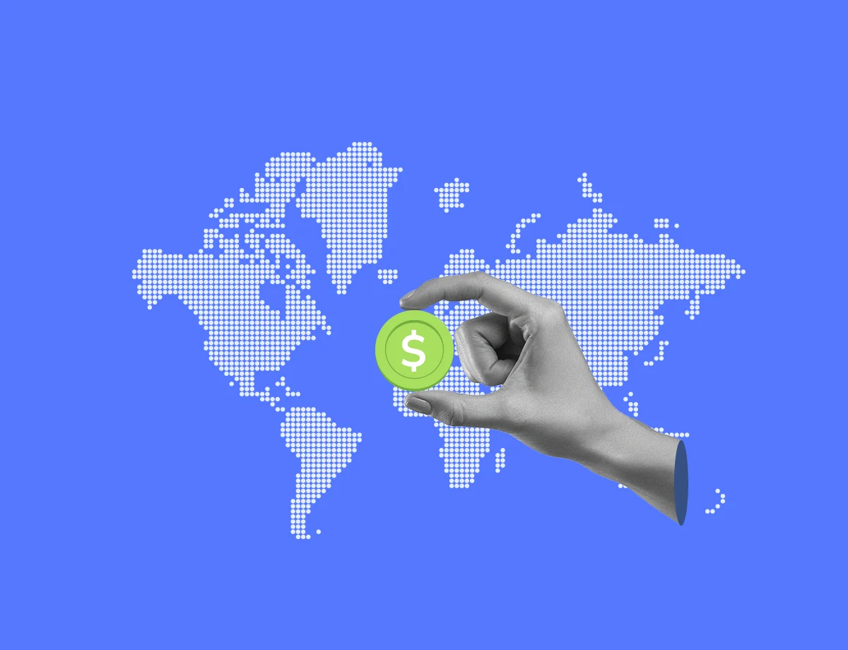 A map of the world with a blue background while a hand is holding a green coin, simulating an international payment method.