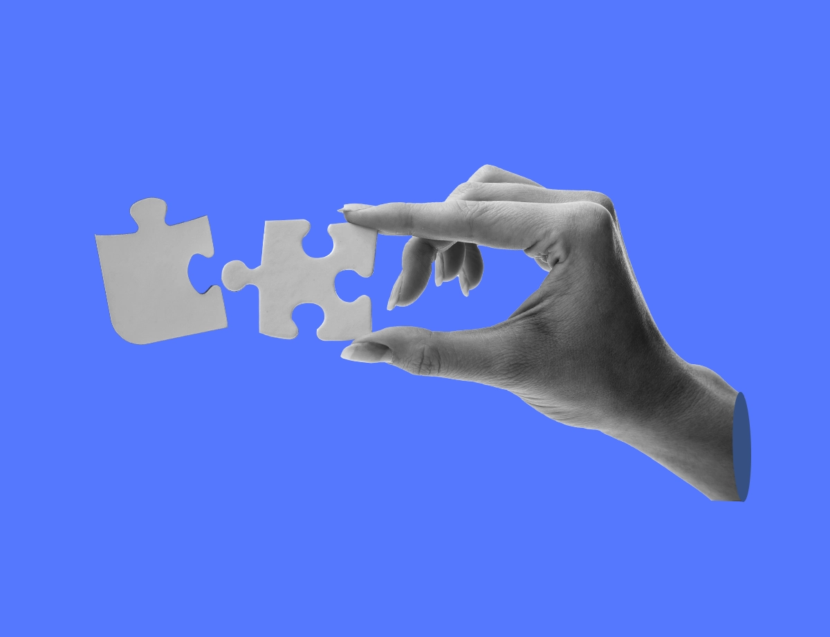 A hand against a blue background holding two interlocking puzzle pieces.