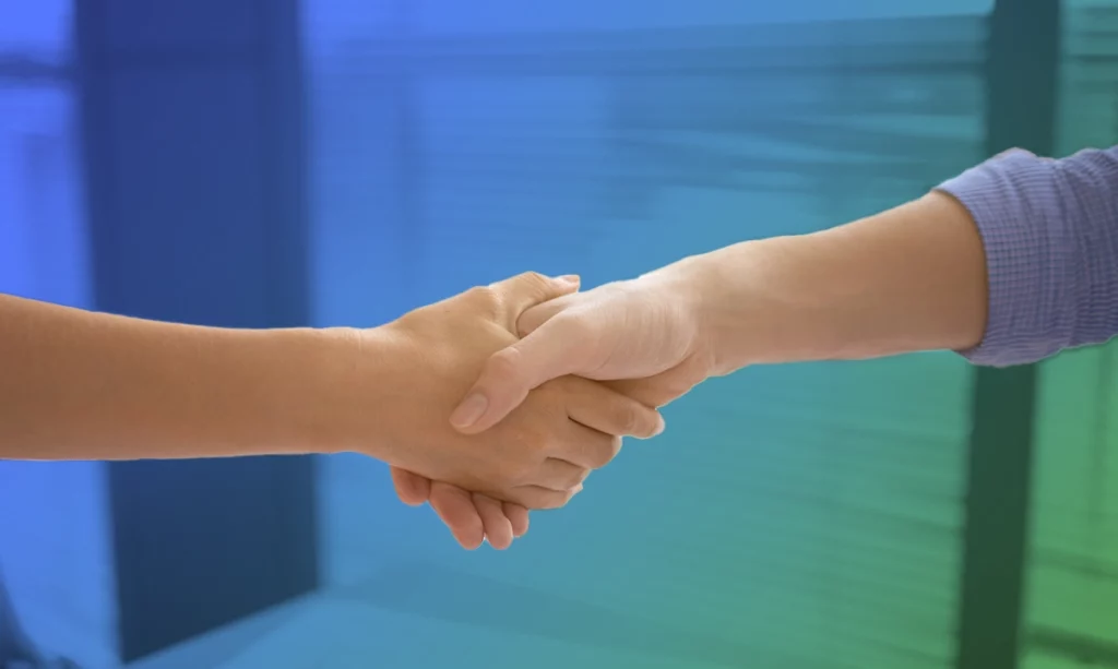 A close-up of two people in a professional setting engaging in a handshake, which represents a mutual agreement or a greeting.